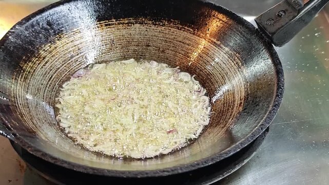 Deep-frying sliced shallots in hot oil to make crispy fried shallots.
