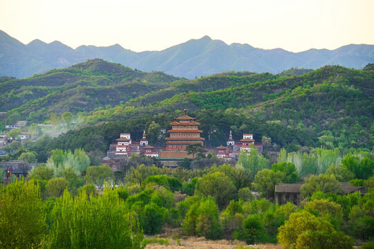 Distant panoramic view of the Mahayana Hall complex at Puning Temple surrounded by lush green forest and mountains at twilight, Chengde, Hebei, China