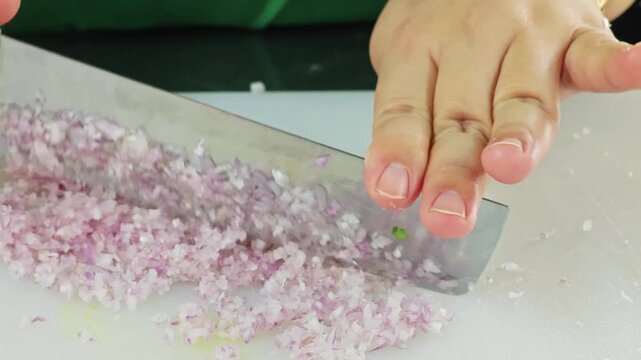 Finely mincing fresh shallots on a white cutting board.