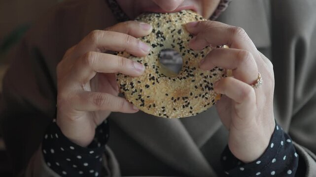 Woman enjoys sesame bagel in a cafe during the daytime
