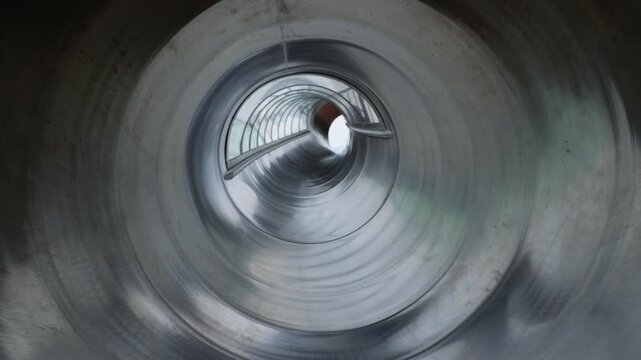 Looking through a shiny metallic pipe structure at a playground.