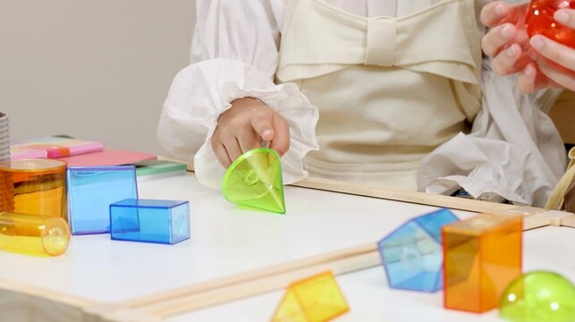 Child Arranging Translucent Colorful Geometric Shapes on a White Tabletop