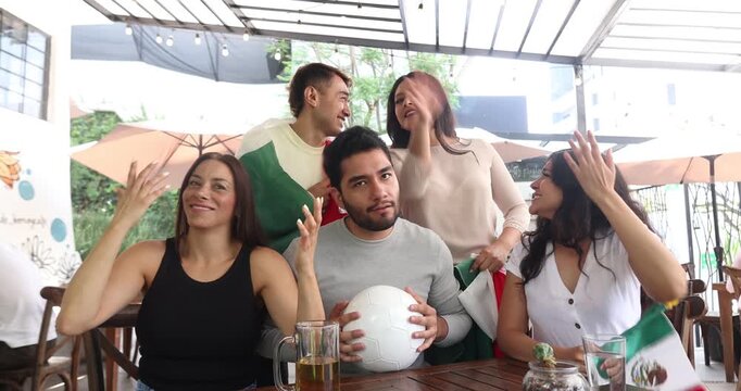 latin people soccer fans watching and cheering a match game with goal, victory or winning championship in a terrace pub. Group of mexicans friends holding a flag in celebration at bar together