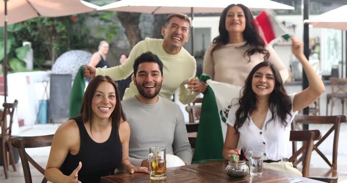 latin people soccer fans watching and cheering a match game with goal, victory or winning championship in a terrace pub. Group of mexicans friends holding a flag in celebration at bar together