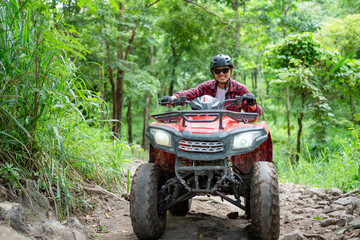 Fototapeta premium Riding an ATV on a dirt trail in the forest with trees and greenery around during the day