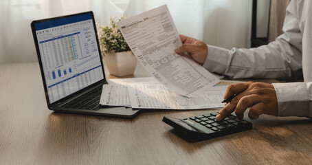 Accountant reviewing financial report and tax documents on laptop while using calculator for account analysis, real estate investment planning, expense management, and reporting workflow. © onephoto