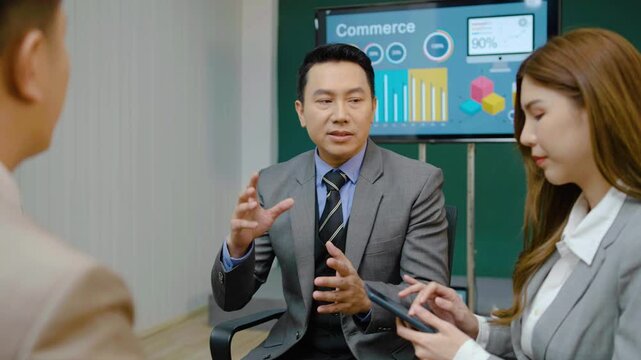 Asian corporate team analyzing commerce data in a boardroom. Professional manager discussing financial graphs on screen during a business meeting. Corporate strategy, teamwork, and leadership.