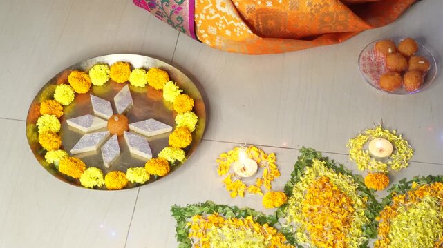 Happy Diwali.Indian woman preparing puja thali with  flowers, rangoli, sweets, mithai like Kaju Barfi, dry fruits and clay diya for Diwali or any other festivals and puja in India. selective focus.