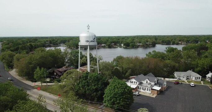 Moving aerial drone video of a water tower in front of a lake somewhere in the midwest on a gloomy day.
