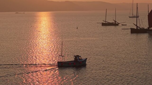 Aerial view of traditional fishing boats and sailboats anchored on the shimmering water during a golden sunset with misty hills in the background Looe, England, United Kingdom.