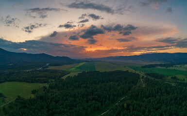 Fototapeta premium Sunset over a winding road through evergreen forests and green fields in the Altai Mountains