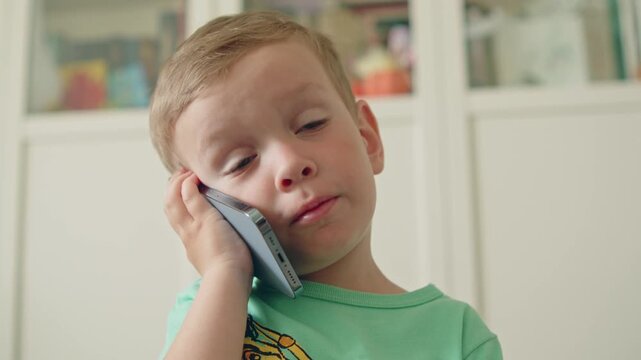 Cute little boy talking with a smartphone to his ear. Small baby boy on a phone call with a modern phone. Happy kid talking on the phone with family and relatives.