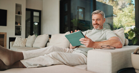 Fototapeta premium Streaming, relax and man on couch with tablet, movie binge and video watching on digital app. Smile, comfy or mature person in house with tech, series subscription or search on entertainment platform