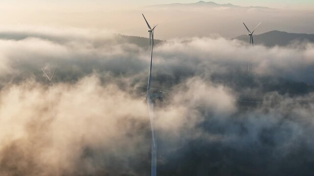 Aerial view of Windpark Freilanderalm wind turbines emerging from thick fog and clouds in the mountains of Pack, Steiermark, Austria.