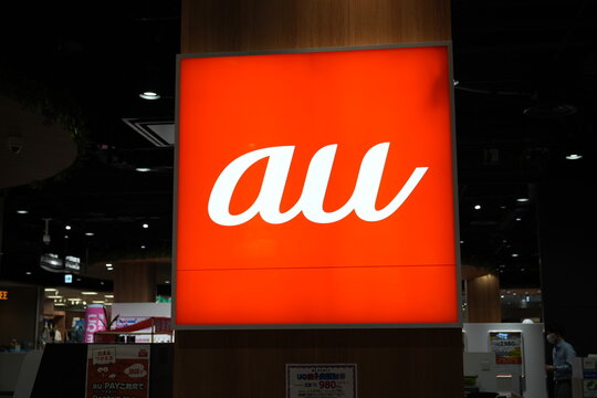 A glowing orange au telecommunication logo sign inside a Japanese store.