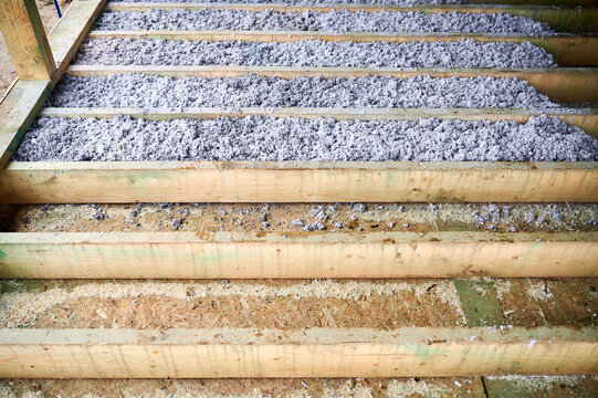 Cellulose paper insulation partially fills floor cavities of timber frame house during installation. Unfinished home construction detail, eco thermal material and energy efficiency concept