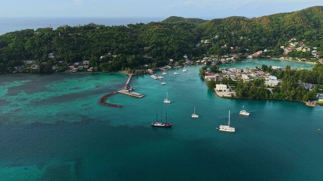 Aerial view of Praslin Ferry Harbour with sailboats anchored in turquoise water surrounded by lush green hills in Baie Ste Anne, Baie Sainte Anne, Seychelles.