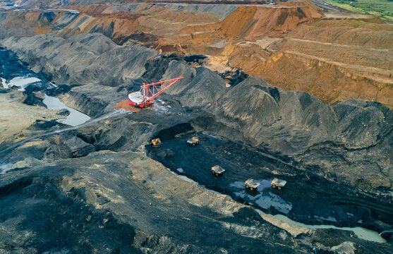 Aerial panoramic view captures industrial scale coal mining operation featuring large dragline excavator and multiple haul trucks