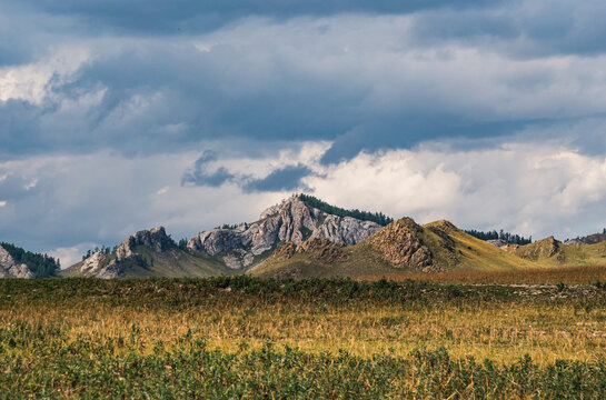 Mountain landscape in Altai features rocky peaks emerging from rolling hills beneath a cloudy sky