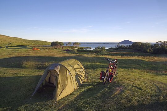Tunnel tent and touring bike on spacious meadow, lake in the background, Myvatn, Iceland