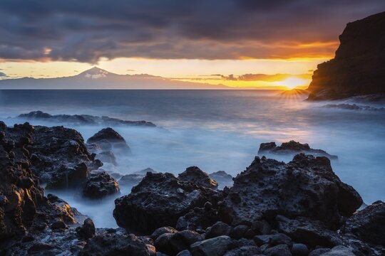 Sunrise on the beach at San Marcos. Rocks, sea and the sun. Tenerife and the Teide in the background. Long exposure. La Gomera, Canary Islands, Spain