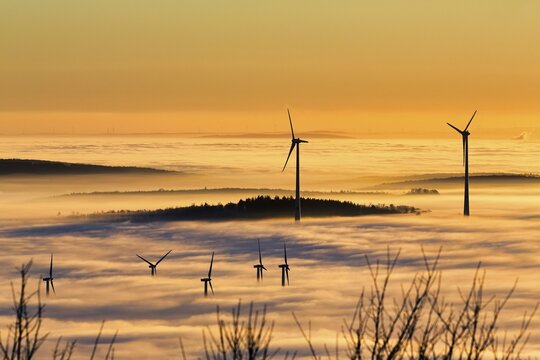 Wind turbines and forest rising from cloud cover, wind power station, bare branches in winter, silhouettes at sunset, K&ouml;terberg, L&uuml;gde, Weserbergland, North Rhine-Westphalia, Germany