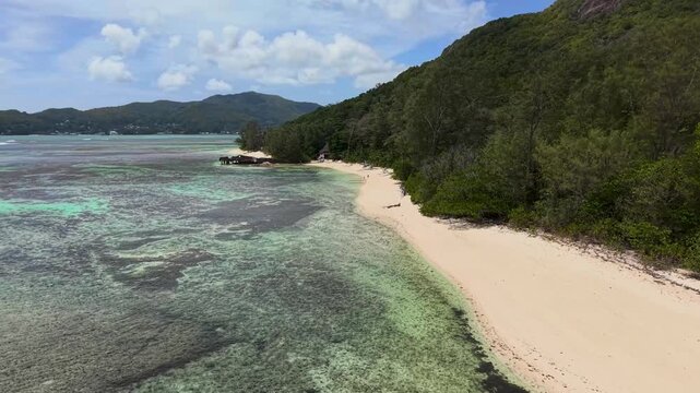Aerial view of the white sandy beach and turquoise waters of Praslin island with lush green hills and coral reefs Round Island, Praslin, Seychelles.
