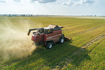 Fototapeta premium Aerial view captures combine harvester working in a vast agricultural field during a sunny daytime harvest, kicking up dust