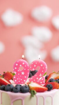 Birthday cake candle number 92. Vertical video of candle and cake on pink background and fire by lighter. Close-up and slow motion