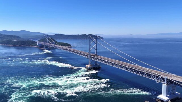 Aerial view of a scenic coastal highway leading to the Onaruto Bridge in Japan. Surrounded by lush greenery and the vast blue ocean, this shot is perfect for driving, travel, and infrastructure themes