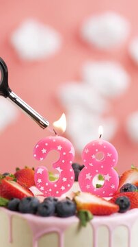 Birthday cake candle number 38. Vertical video of candle and cake on pink background and fire by lighter. Close-up and slow motion