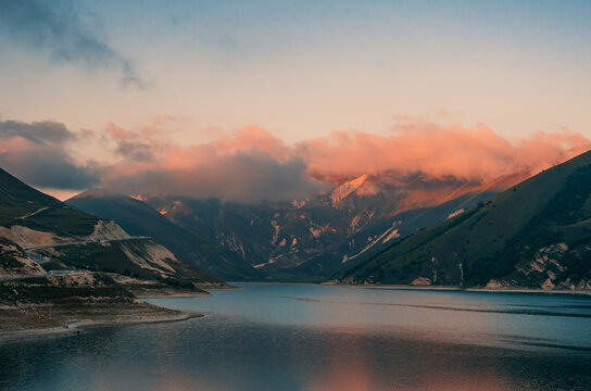 Aerial view captures expansive Lake Kazenoy-Am nestled between steep green mountains under a sunset sky