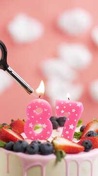 Birthday cake candle number 87. Vertical video of candle and cake on pink background and fire by lighter. Close-up and slow motion
