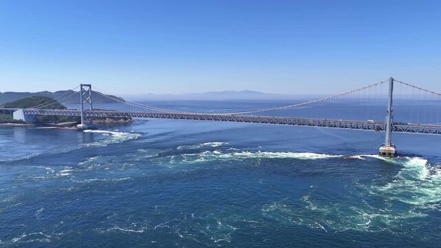 A breathtaking 4K aerial establishing shot of the Onaruto Bridge over the Naruto Strait. The wide-angle perspective captures the vast ocean, distant islands of the Seto Inland Sea, and a clear blue sk