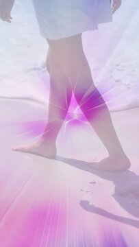 Vertical video: Sun urging bare feet walking shore, leaving prints while waves washing pink glow