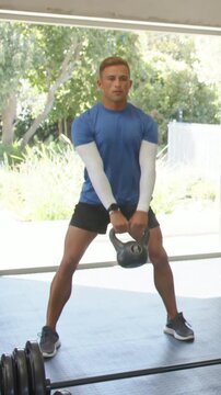 Vertical video: Swinging man in blue shirt driving hips in garage with kettlebell for training