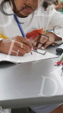 Vertical video: Boy taking blue pencil, writing classwork in class with letters drifting over page