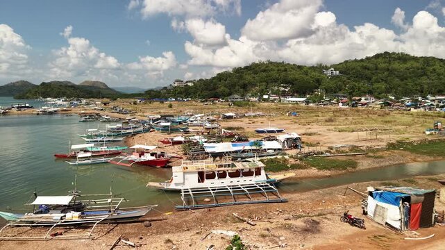 Beached outrigger boats on a sandy shoreline in Coron Palawan Philippines with calm bay water green hillside village small huts and bright tropical clouds