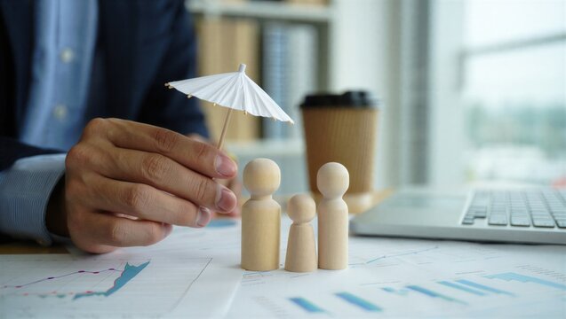 Life insurance concept showing family protection with wooden figures under umbrella on financial documents. Represents coverage, beneficiaries, income security, financial planning.