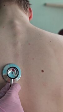 Doctor checks patient back with stethoscope in clinic setting during daytime
