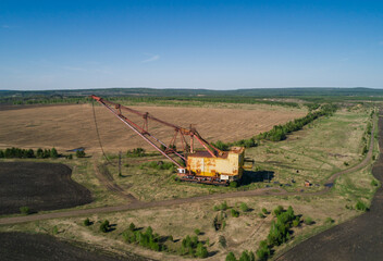 Fototapeta premium Massive industrial dragline excavator rests in an open field, surrounded by sparse vegetation and dirt roads