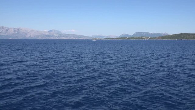 Sailboat on Calm Blue Sea with Mountain Coast Horizon.