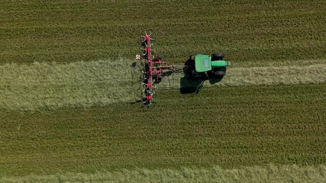 Aerial View of Tractor Cultivating Field: A green tractor with an attached cultivator works across a vast, freshly cut grassy field, creating neat rows.