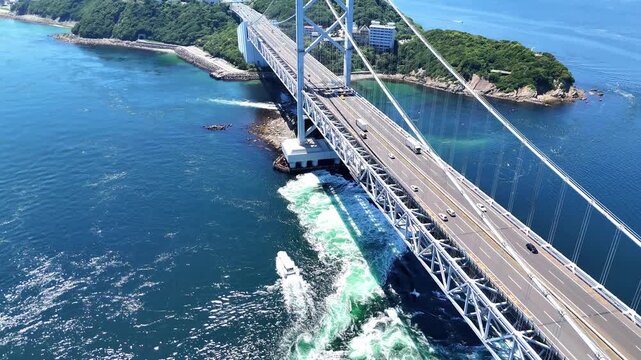 Epic 4K aerial panorama of the Onaruto Bridge connecting beautiful green islands in Japan. Features highway traffic, massive infrastructure, and dynamic ocean currents of the Naruto Strait under a cle