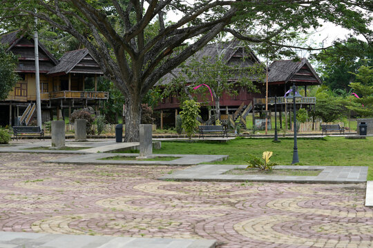 Traditional wooden stilt houses surrounded by large trees and green park scenery, creating a peaceful and natural atmosphere in a public outdoor space.