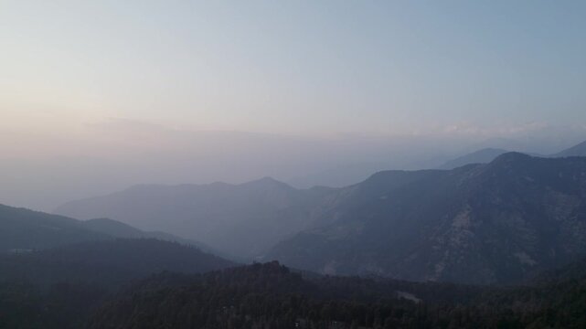 Aerial view of the misty mountain ranges of Chopta Tungnath with layered silhouettes under a soft sunrise sky Chopta, Uttarakhand, India.