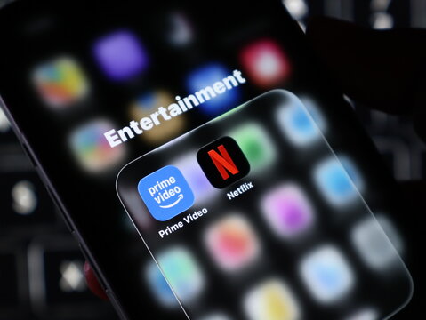 Closeup of a smartphone screen showing an entertainment folder with prime video and netflix apps, with a blurred background