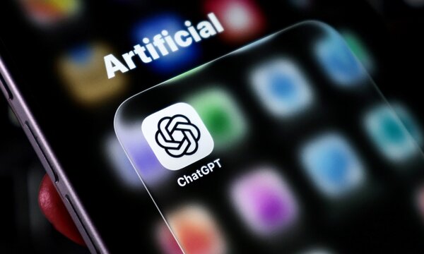 Closeup of a smartphone screen displaying the chatgpt app icon with the word artificial visible in the background