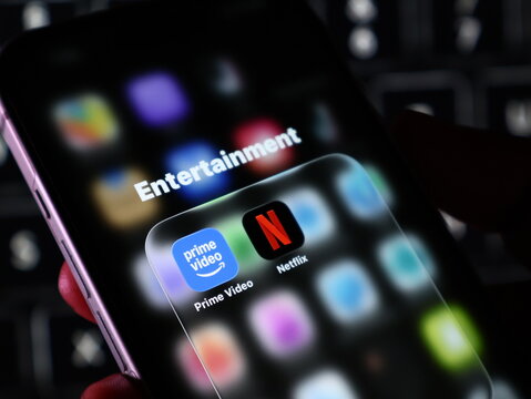 Closeup of a smartphone screen showing an entertainment folder with prime video and netflix apps, held in a hand against a dark background