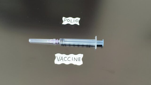 Polio, poliomyelitis or poliovirus childhood disease in children prevention and protection immunity vaccination or IPV injection concept. Hand placing syringe near polio vaccine word or text.